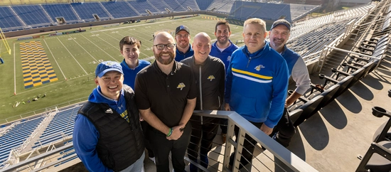 jackrabbit sports network group smiling together with the dana j dykhouse football field in the background