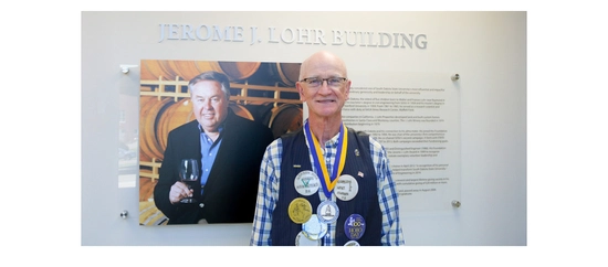 Gordon Niva smiling in front of a sign that displays a photo of Jerry Lohr