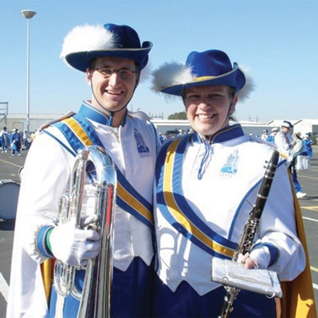 alex halbach in his pride of the dakotas uniform standing smiling with another member, both holding instruments