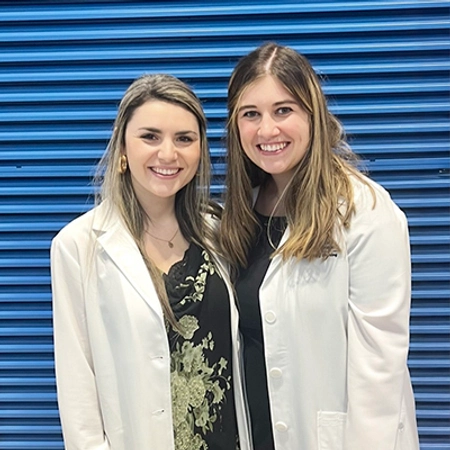 Hanna smiles with another friend, both dressed in their nursing white coats