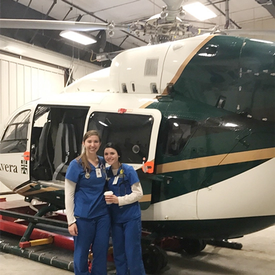 Hanna smiles with another nursing student, in front of a helicopter