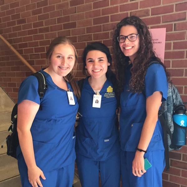 Hanna smiles with two other nursing students, all wearing blue scrubs