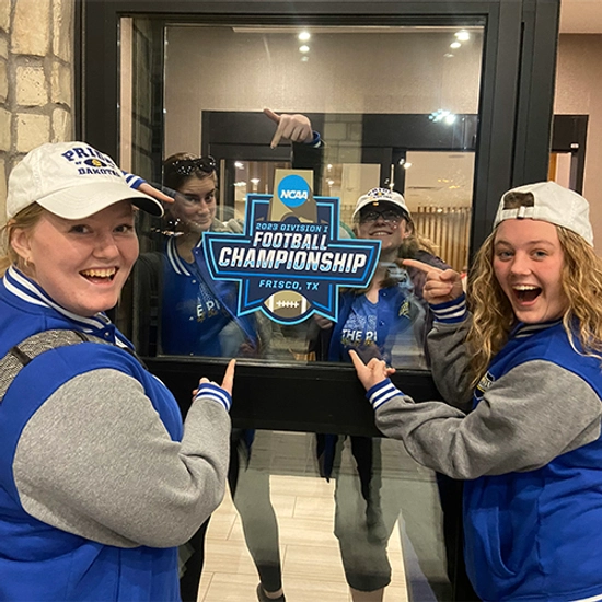 group of four girls in Jacks gear by a 2023 national championship sign