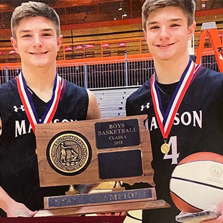Janke twins in their junior high years with medals around their necks holding a basketball trophy, smiling