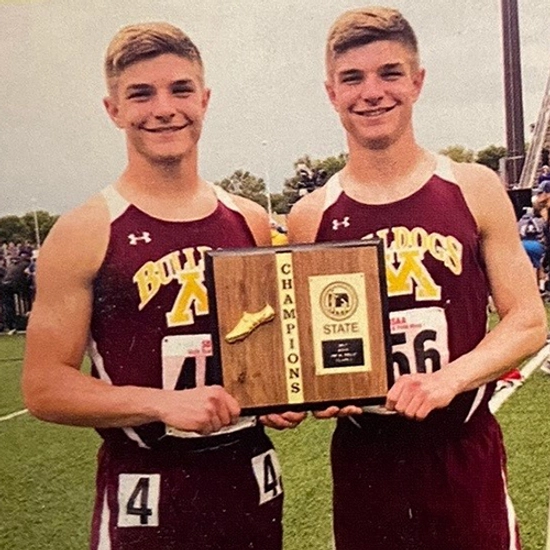 Janke twins in their track uniforms, standing together holding a track trophy
