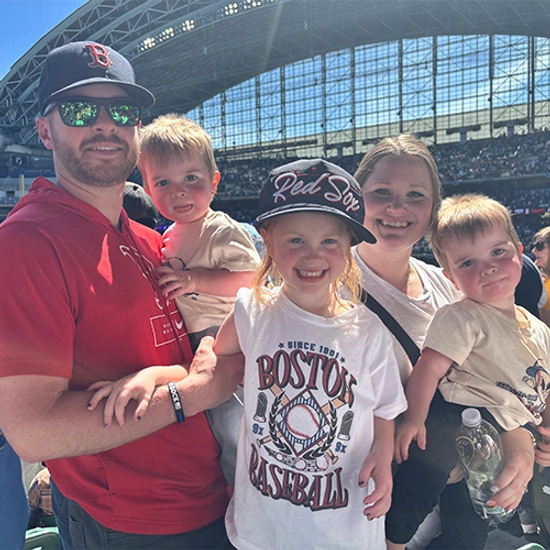 Jillian Baldini, her husband, and three children smiling for a photo at a Boston Red Sox game.