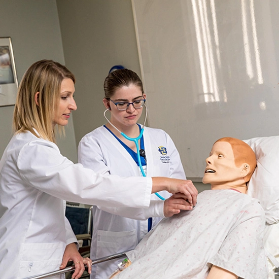 SDSU professor helps a female nursing student listen to a mannequin patient's heart beat.