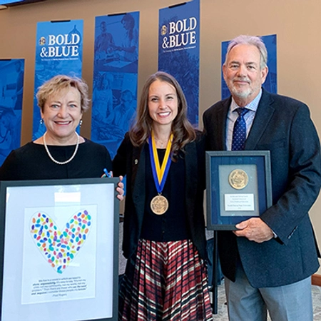 Mary DeJong holding a personalized gift, Dr. Carie Green with her medallion around her neck and Tate Profilet holding a framed medallion all smile for a photo after the investiture ceremony.