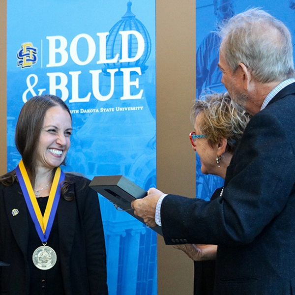 Dr. Carie Green smiles at Tate Profilet and Mary DeJong as they hold their framed medallion.