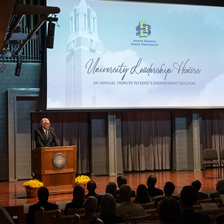 President Dunn speaks on stage at a podium to a crowd at the university leadership honors event