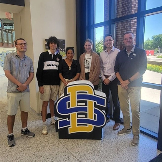 The Wintrode family stands with SDSU faculty and representatives behind a large SDSU logo sign.