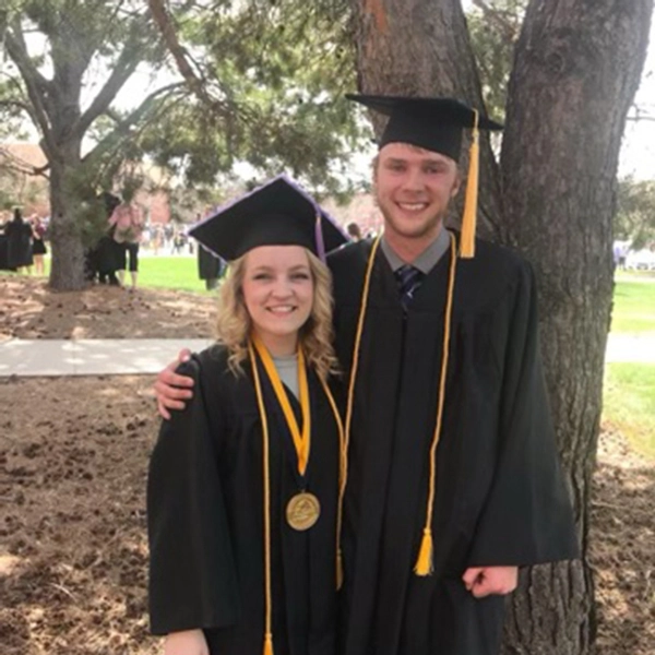 Sydney and Nathan smile after convocation, both dressed in their graduation cap and gown attire.