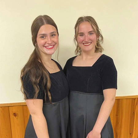 Two ladies from the SDSU choir stand by each other smiling in their choir gowns