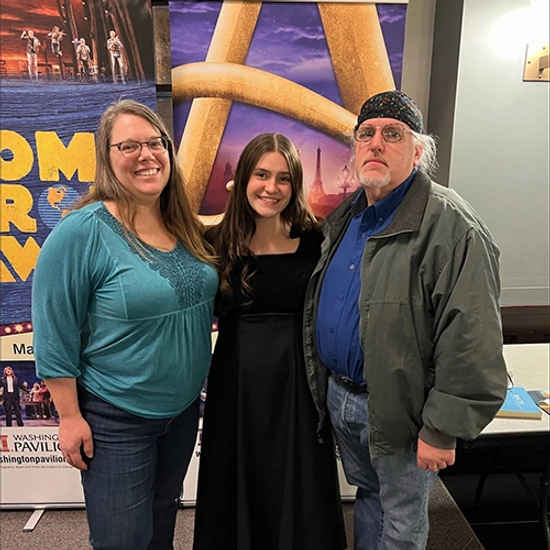 Arianna stands smiling with her parents on either side of her