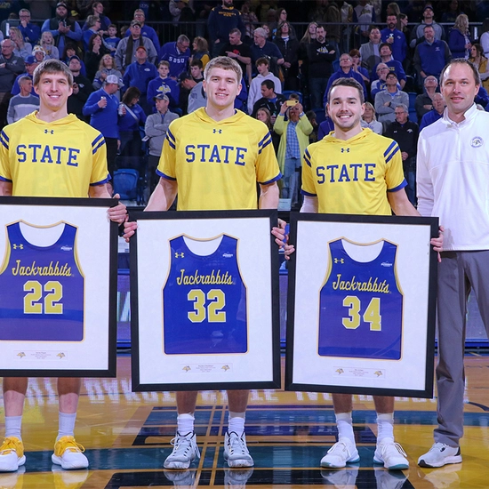 alex arians stands with other sdsu basketball players with their framed jerseys