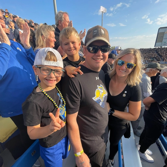 Carolyn and her husband and two sons smiling at a Jackrabbit football game.