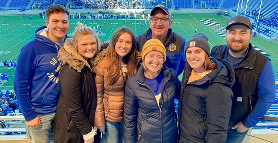 A photo of Marc and Julie Mooney in a football suite with their children at an SDSU football game at Dana J. Dkyhouse Stadium.