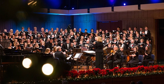 full sdsu concert choir on stage singing with red poinsettias and holiday trees