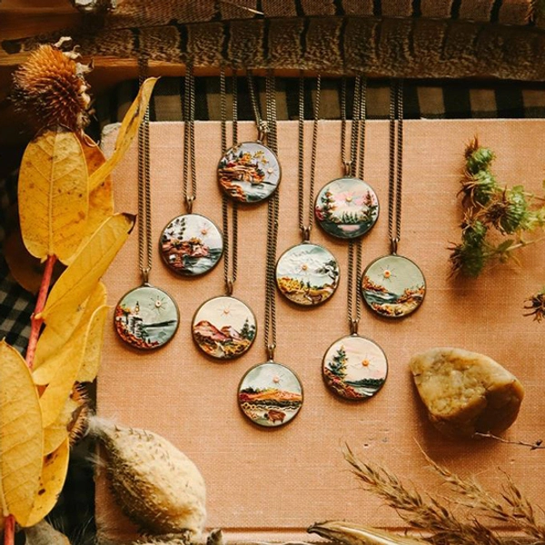 Closeup of 9 earth clay necklaces on chains with some earthy foliage around it
