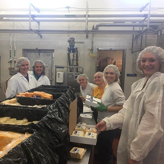 Group of six SDSU dairy students, standing around a table, filling cheese boxes.