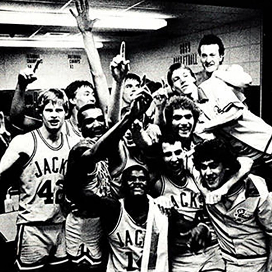 A Black and white photo of the men's Jackrabbit basketball team celebrating in the locker room of Frost arena after a win