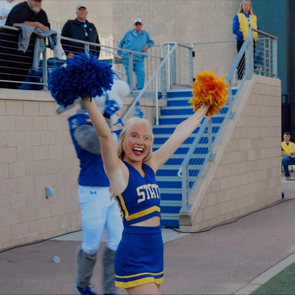 grace stroschein in her sdsu cheerleader outfit with pom poms in hands smiling while cheering at a football game