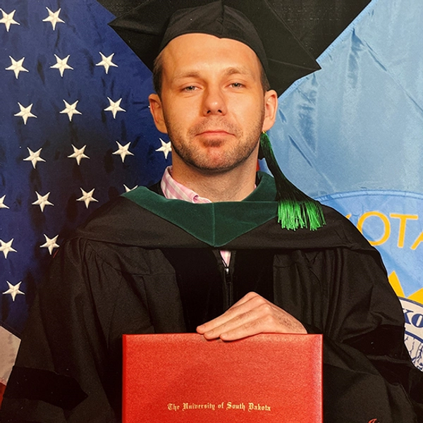 A young gentleman in a commencement cap and gown holding a diploma