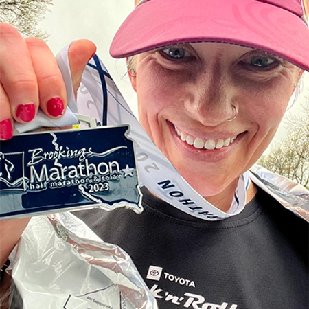 Anne Karabon smiling at the camera, holding up a Brookings Marathon medal.