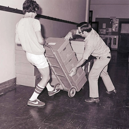 Two people using a dolly to move boxes of books.