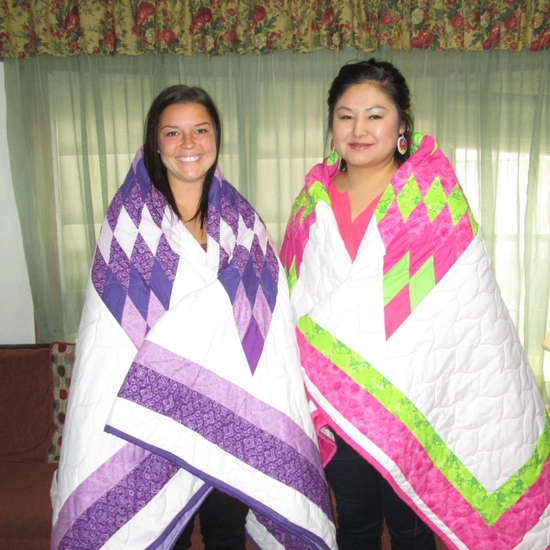 2 female students during their honoring ceremony, wrapped in colorful star quilts
