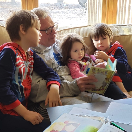 john stiegelmeier sits on a couch reading a book to some of his grandkids