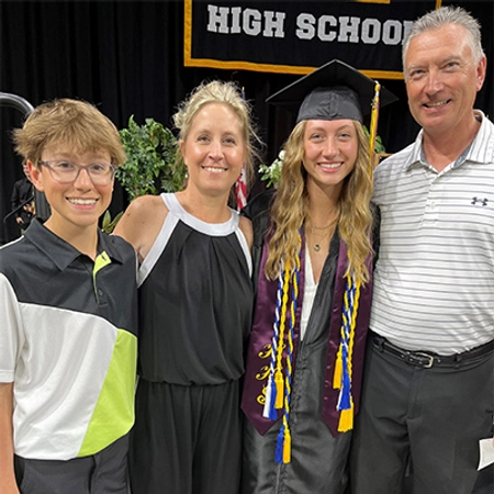 A young lady in a high school graduation cap and gown standing with her 3 family members