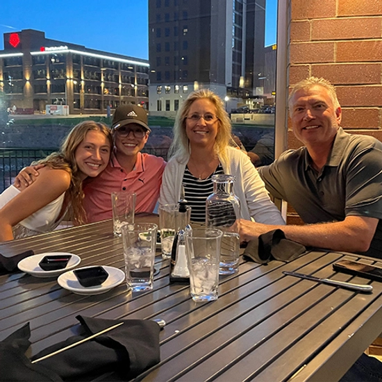 A family of four surrounded at a dinner table smiling for the camera