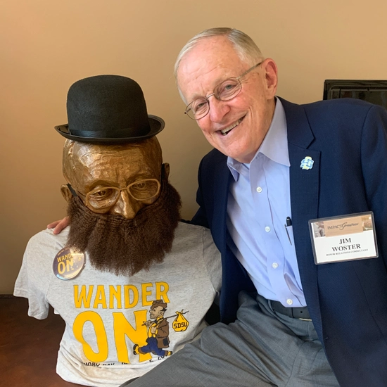 jim woster puts his arm around the bust that was made in his likeness