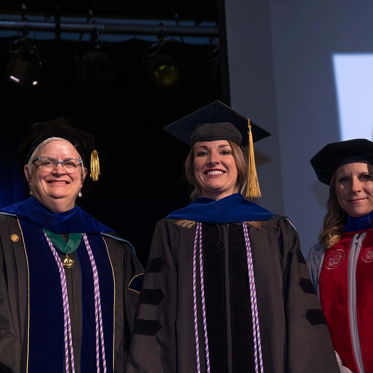 Brittany Brennan receives her nursing doctoral hooding, standing next to two Nursing faculty members.