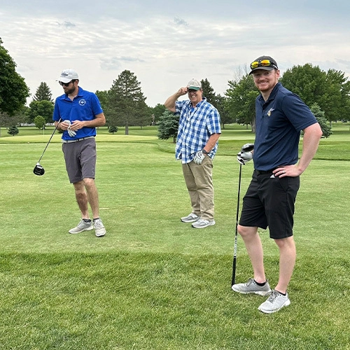 Three men standing on a golf course.