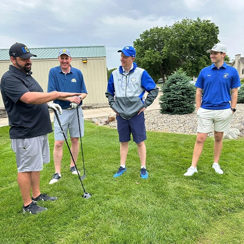 Four men standing on a golf course, smiling and chatting.