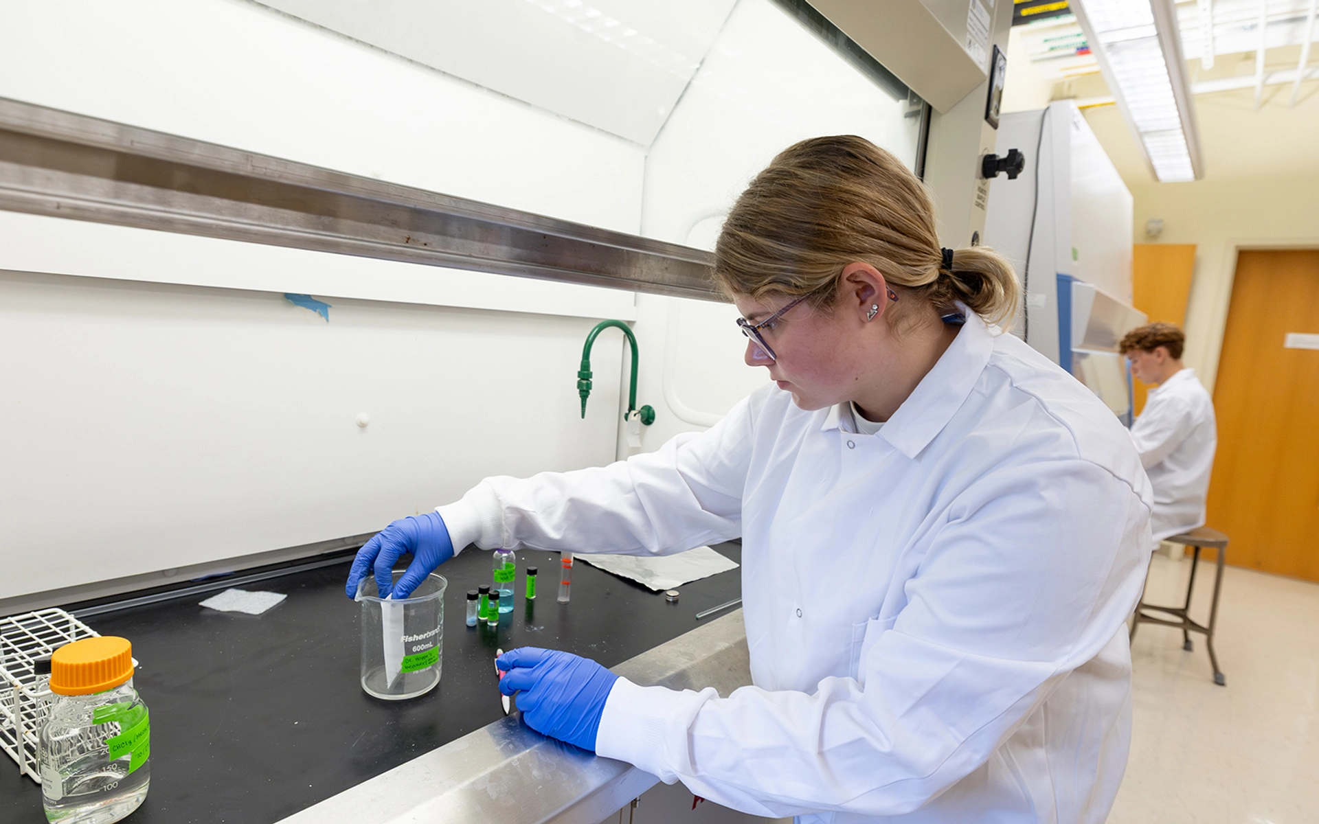 Female lab student wearing a white coat working on an experiment in a lab.