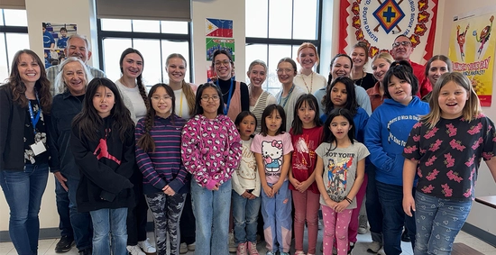 Ten SDSU students stand together in a classroom with a group of young students in Norris Elementary School.