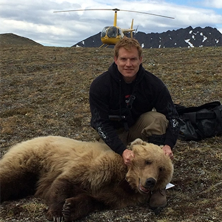 Grant Hilderbrand crouches down to smile near a tranquilized bear