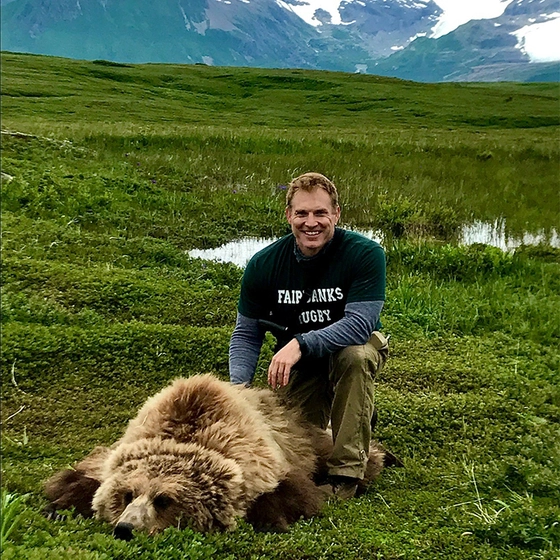Grant Hilderbrand crouches down to smile near a tranquilized bear