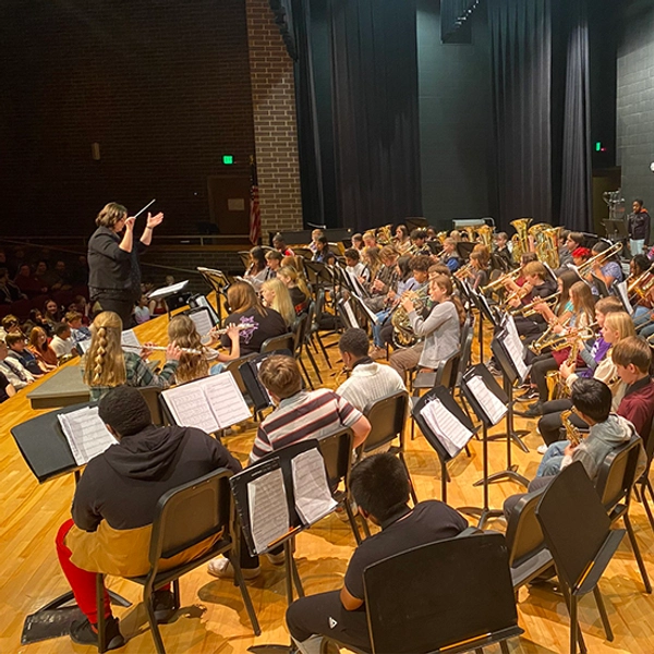 Marian Beck stands on stage while conducting a 6th Grade Band Concert.