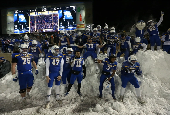 South Dakota State University football players pose on a pile of snow in front of the student section in Dana J. Dykhouse stadium.