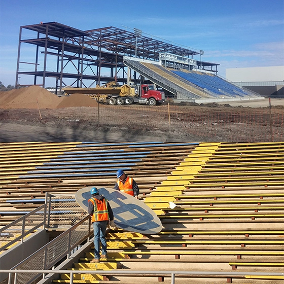 Two workers carry an SDSU sign while a structure is being built in the background.