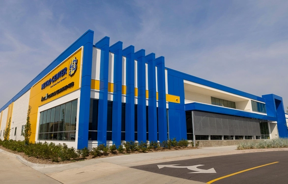 A modern blue-and-yellow commercial building with tall vertical fins and broad glass windows stands beside an empty road under a cloudy sky, creating a bold, orderly impression.
