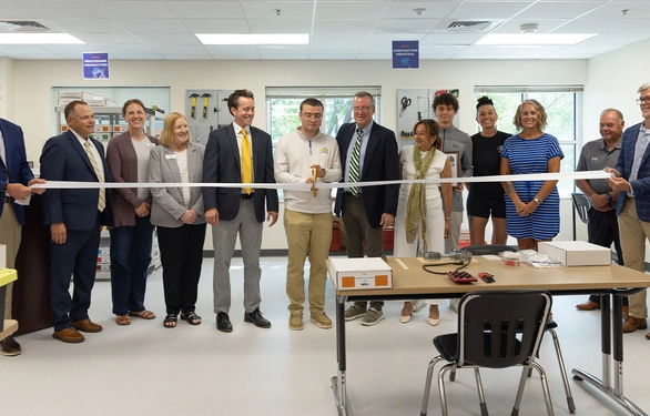 University staff and guests pose behind a ribbon stretched across a classroom, celebrating an opening with smiles and a formal, upbeat tone.