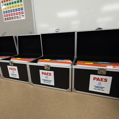 Three open black PAES equipment cases display neatly organized colored materials in a bright room.