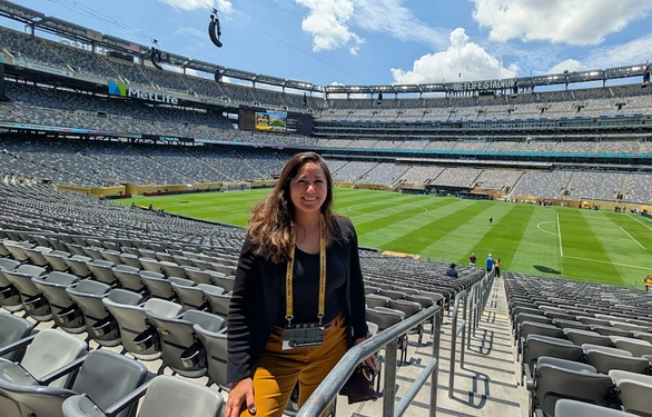 Susanna Marking stands among empty stadium seats at MetLife Stadium overlooking a sunlit soccer field.