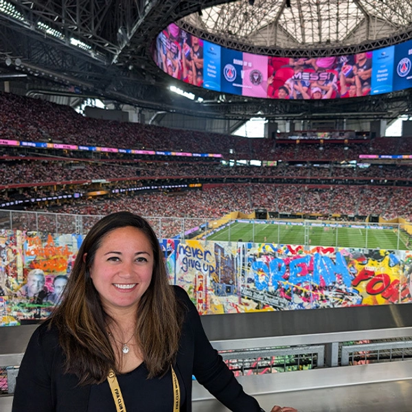 Susanna Marking poses inside a packed indoor stadium, with colorful fan banners, a football field, and giant screens creating an energetic atmosphere.