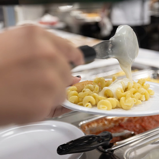 A hand scoops noodles with sauce onto a plate.